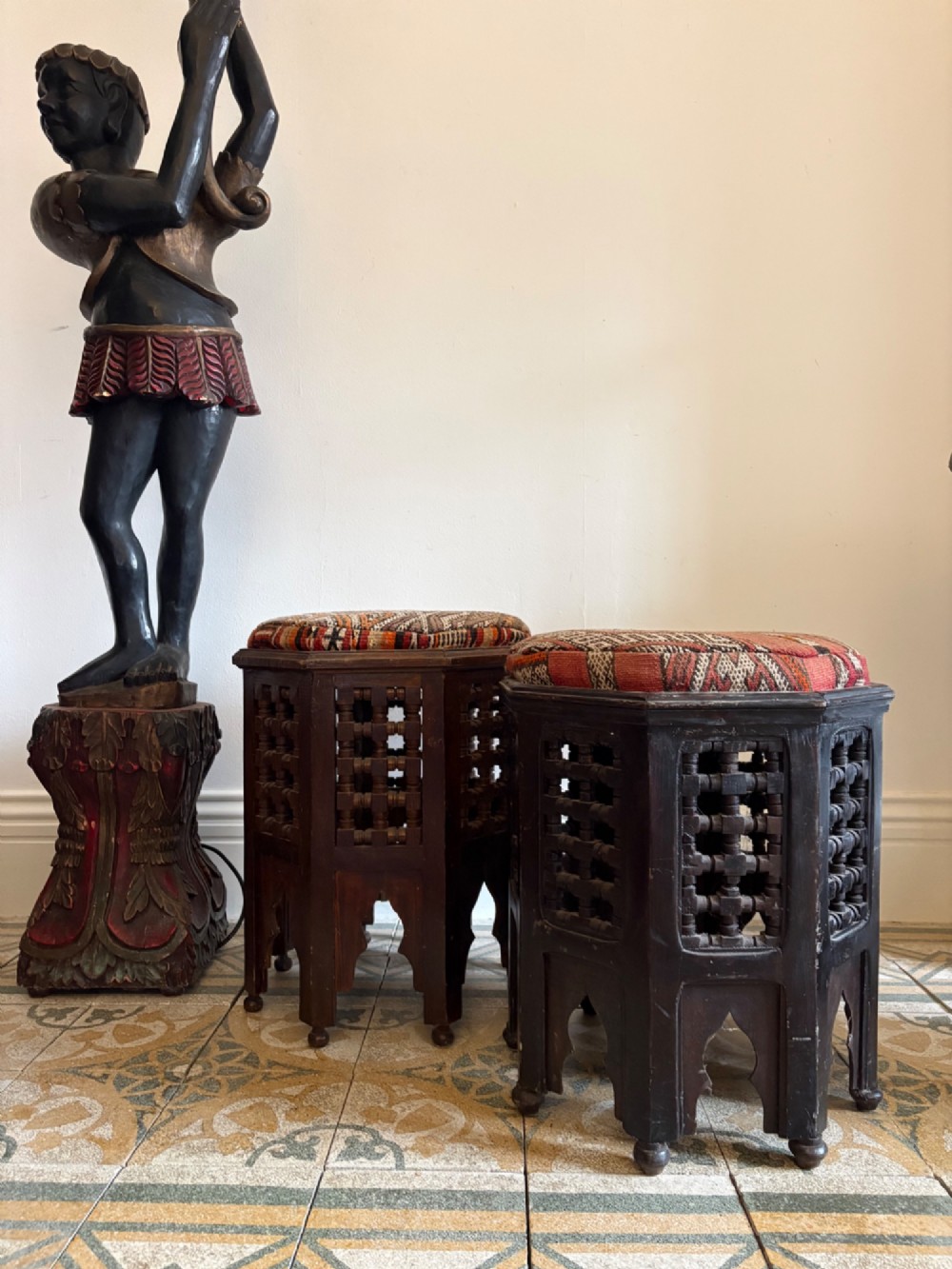 A pair of dark wood octagonal stools with turned latticework side panels, arch-cut bases, and geometric woven kilim seat cushions. View II