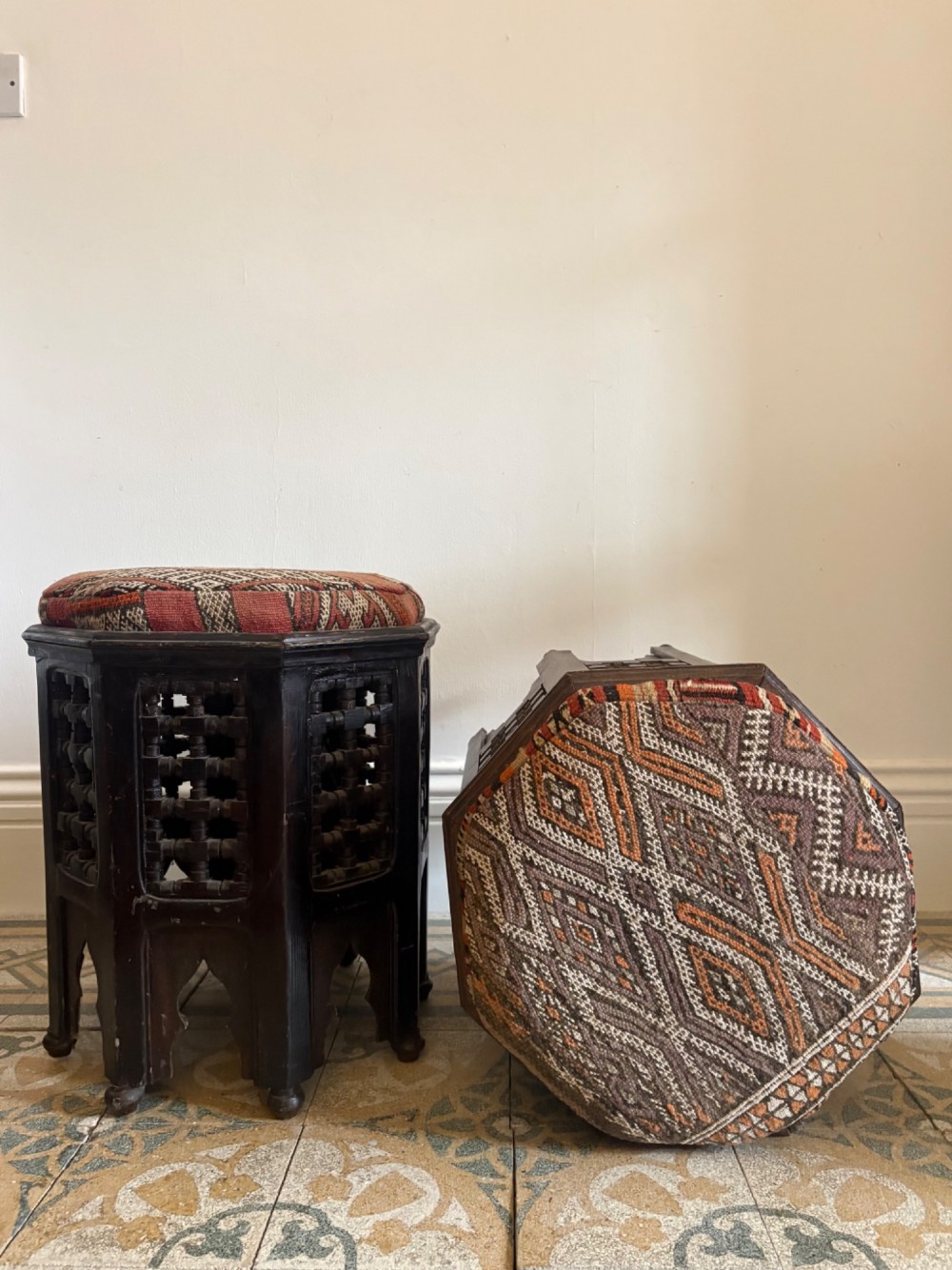 A pair of dark wood octagonal stools with turned latticework side panels, arch-cut bases, and geometric woven kilim seat cushions. View V