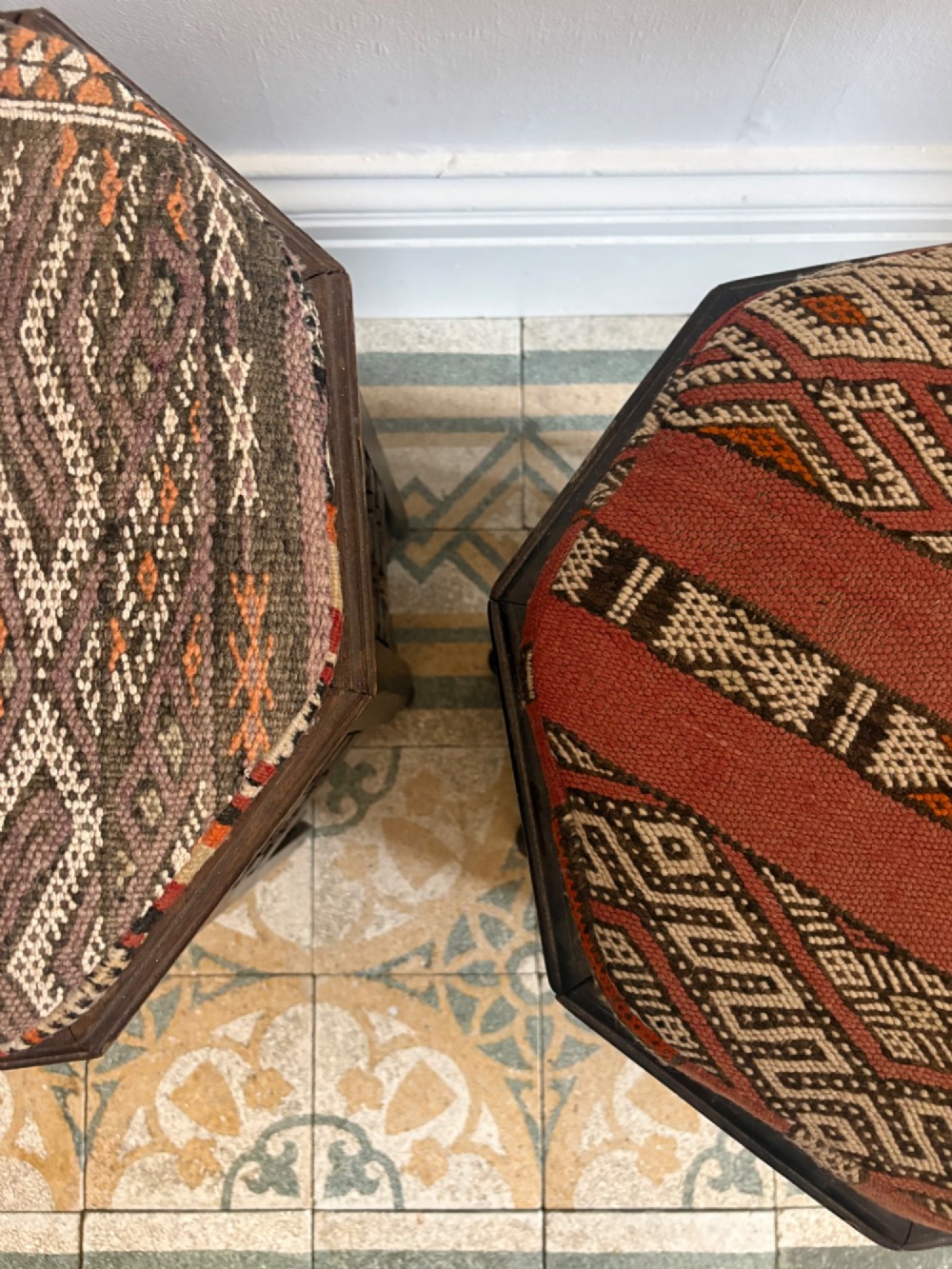 A pair of dark wood octagonal stools with turned latticework side panels, arch-cut bases, and geometric woven kilim seat cushions. View VI