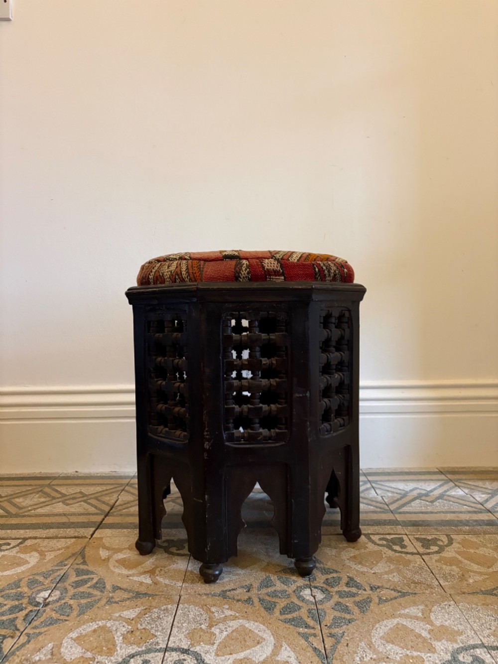 A pair of dark wood octagonal stools with turned latticework side panels, arch-cut bases, and geometric woven kilim seat cushions. View VIII