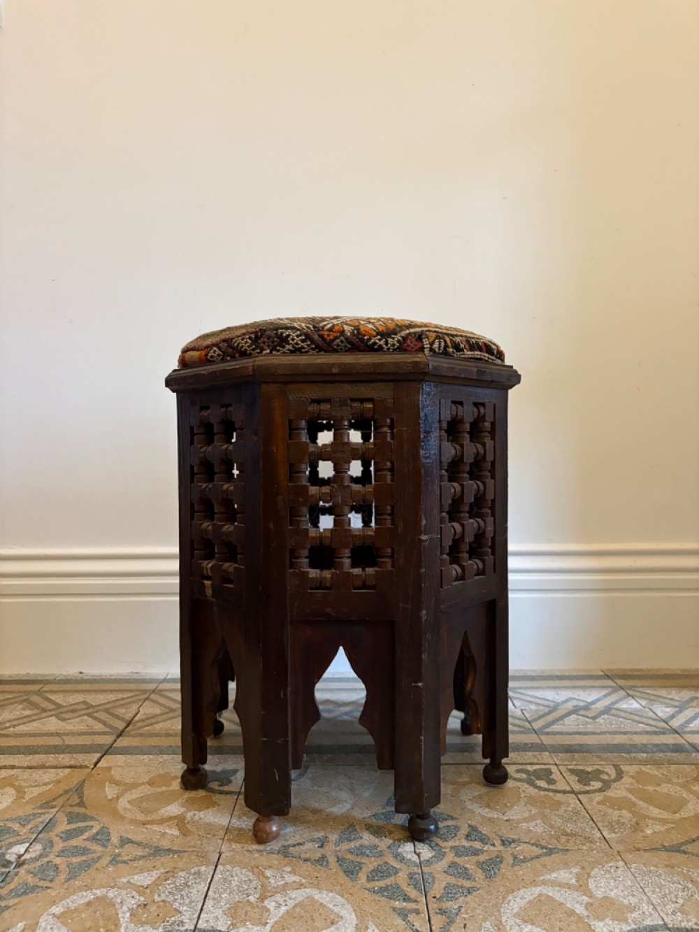 A pair of dark wood octagonal stools with turned latticework side panels, arch-cut bases, and geometric woven kilim seat cushions. View IX