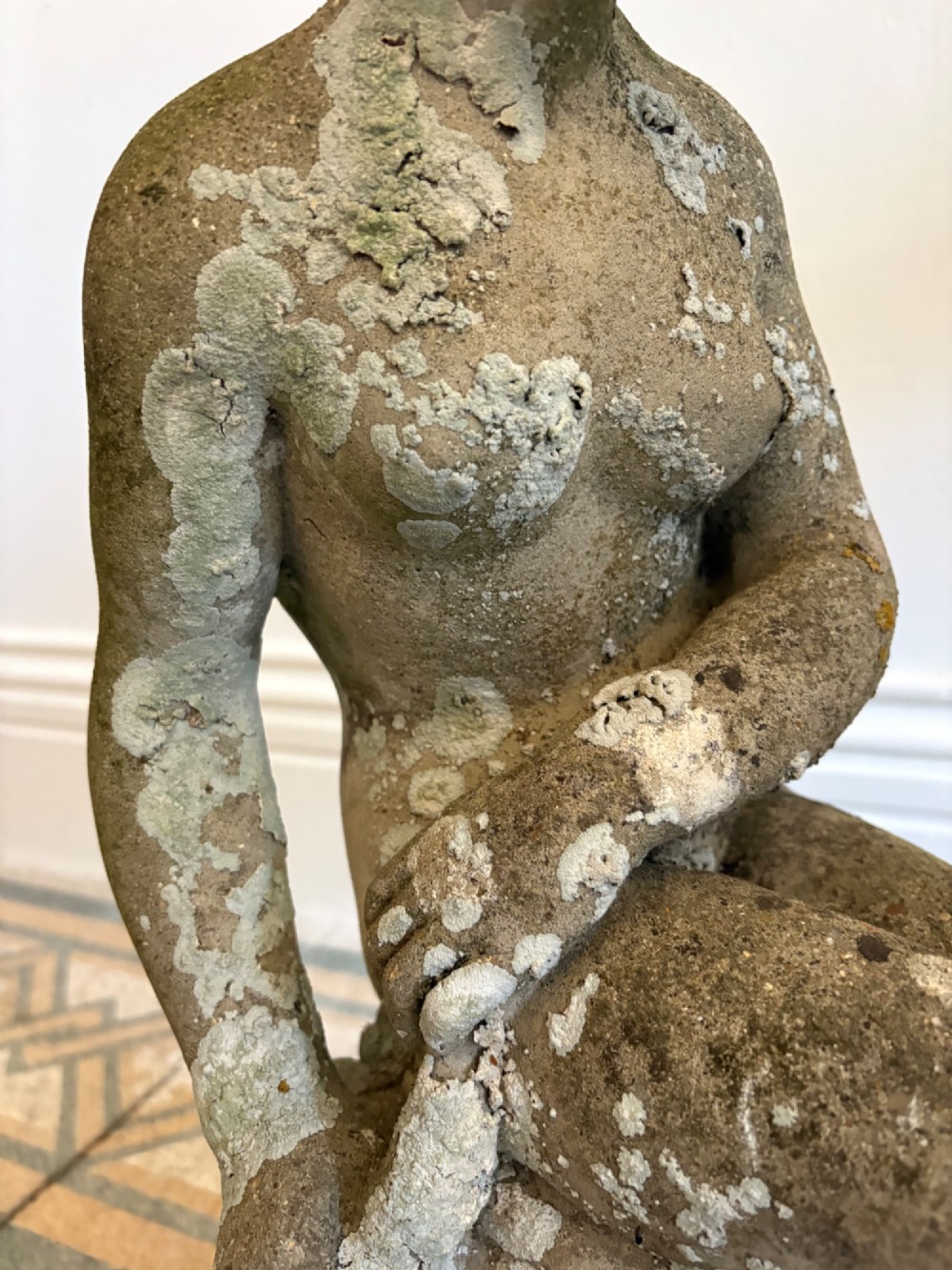 A weathered cast stone statue depicting a seated classical female bather figure with a natural lichen patina. View VIII