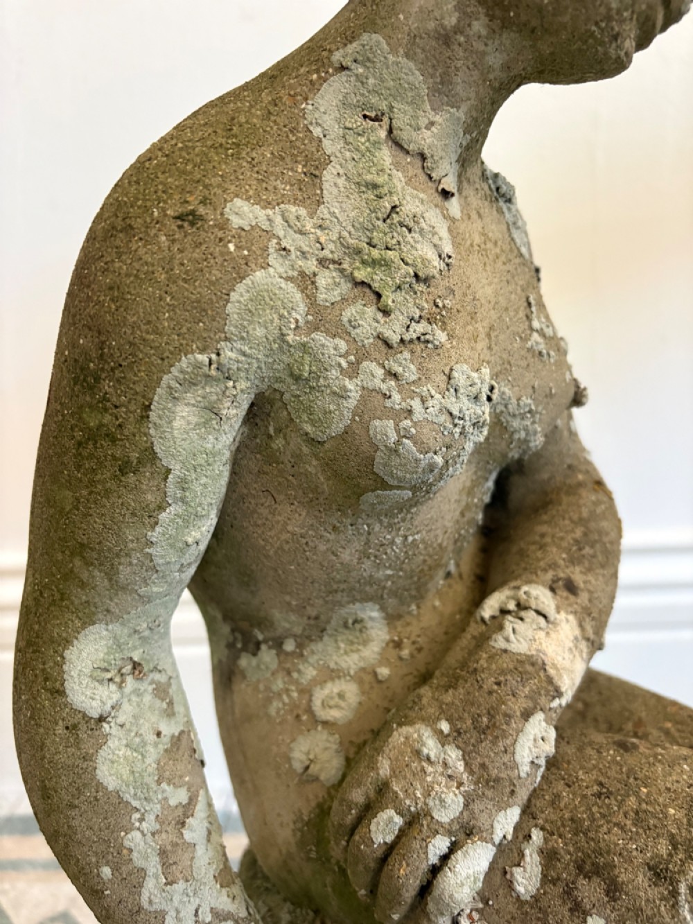 A weathered cast stone statue depicting a seated classical female bather figure with a natural lichen patina. View IX