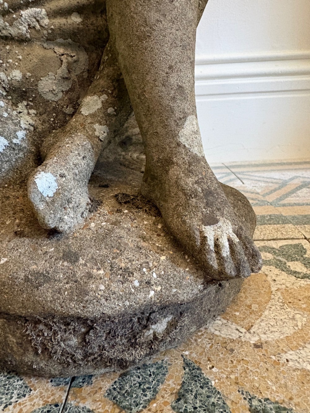 A weathered cast stone statue depicting a seated classical female bather figure with a natural lichen patina. View X