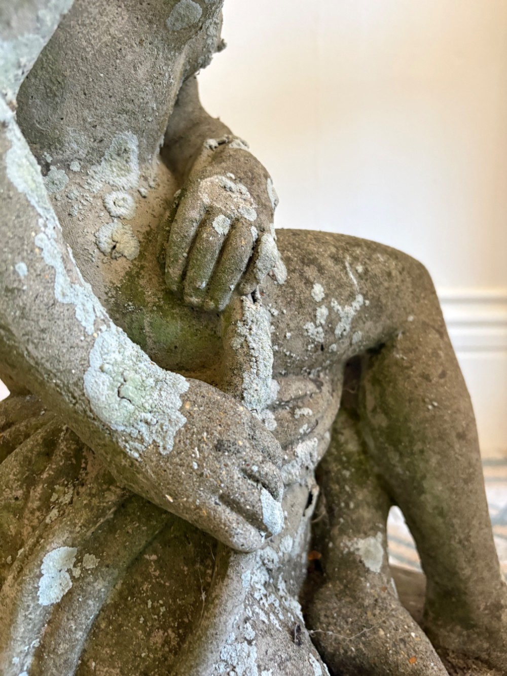 A weathered cast stone statue depicting a seated classical female bather figure with a natural lichen patina. View XI