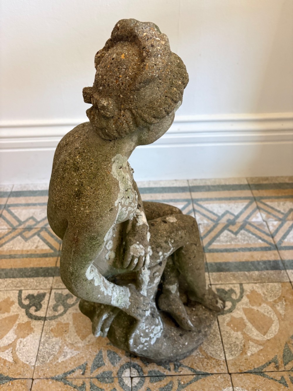 A weathered cast stone statue depicting a seated classical female bather figure with a natural lichen patina. View XII