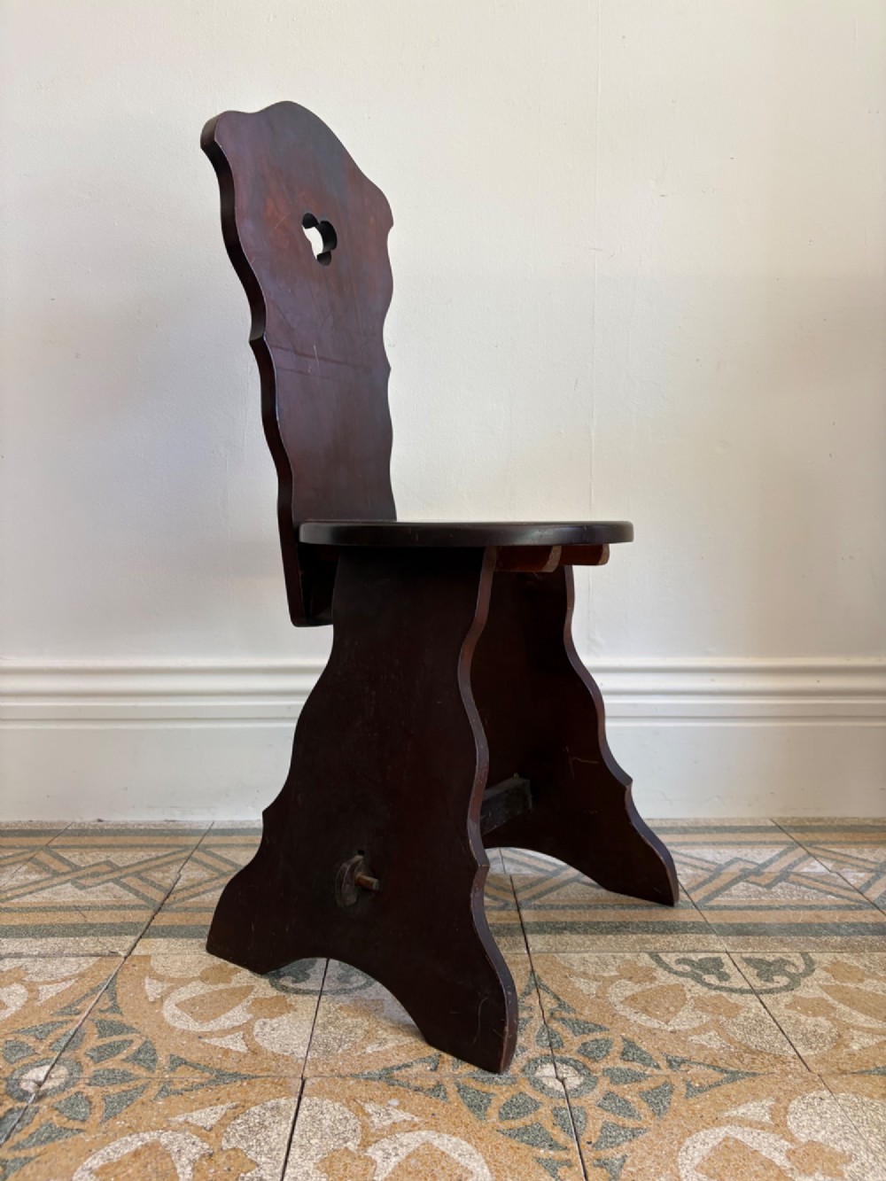 An Arts and Crafts dark mahogany hall chair featuring a shaped backrest with a pierced heart cutout and splayed legs. View VI