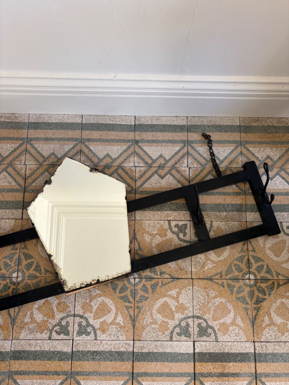 A tall black wrought iron wall-mounted coat rack featuring integrated hooks, hanging chains, and an asymmetrical pentagonal mirror. View II