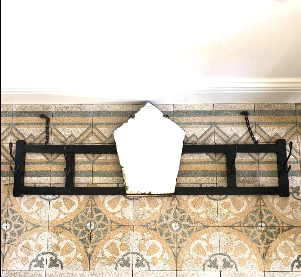 A tall black wrought iron wall-mounted coat rack featuring integrated hooks, hanging chains, and an asymmetrical pentagonal mirror. View III