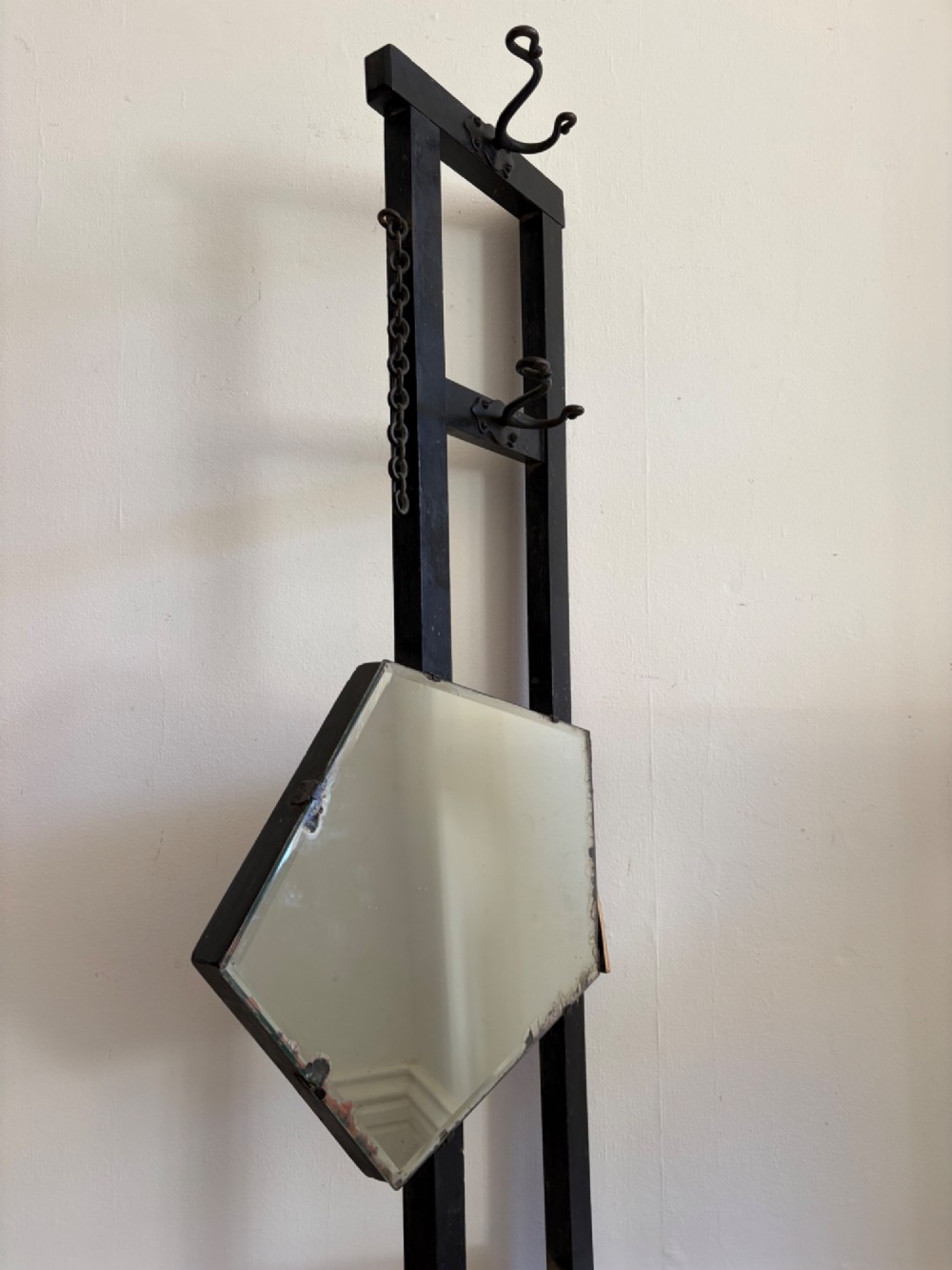 A tall black wrought iron wall-mounted coat rack featuring integrated hooks, hanging chains, and an asymmetrical pentagonal mirror. View VIII