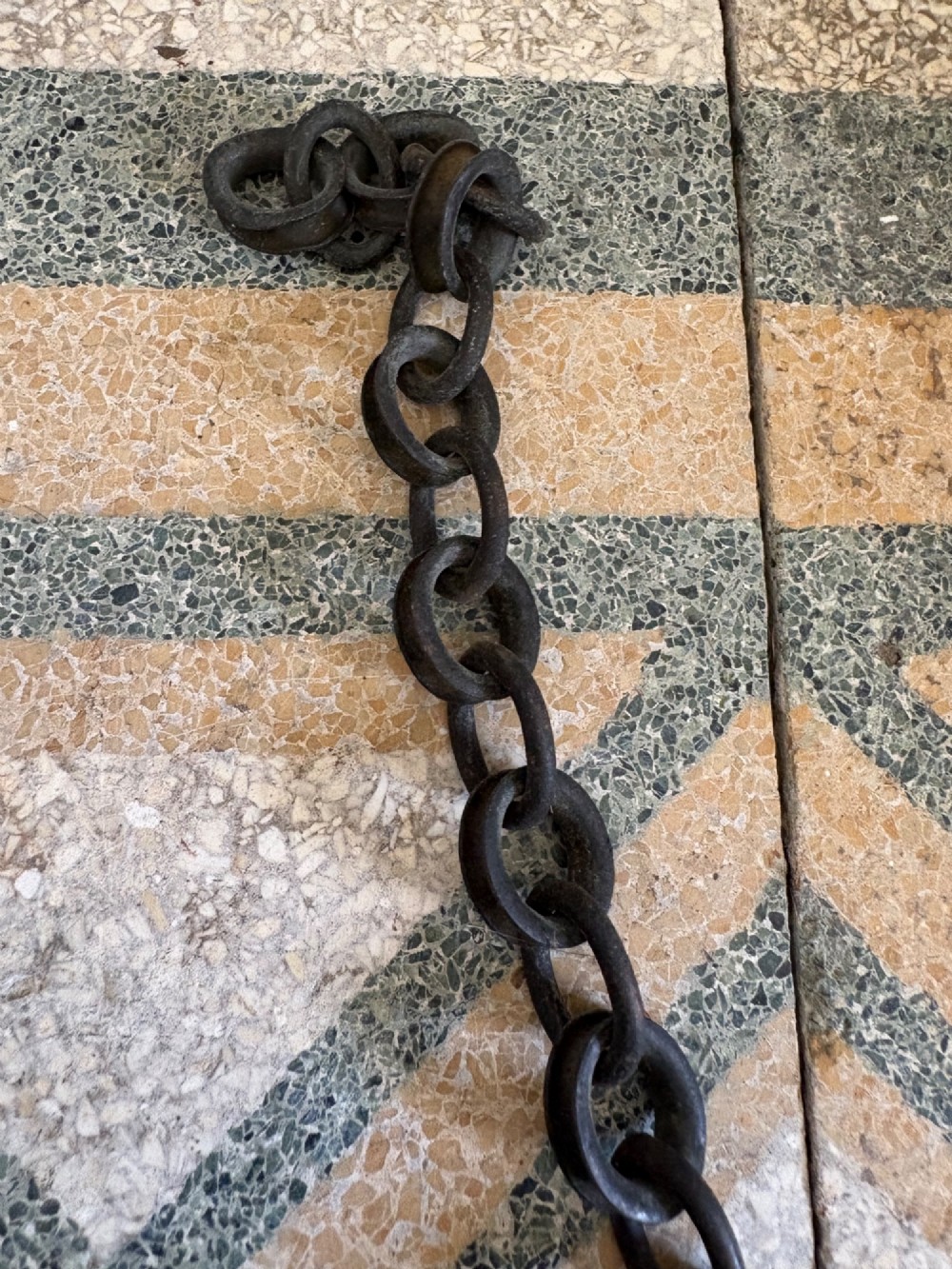A tall black wrought iron wall-mounted coat rack featuring integrated hooks, hanging chains, and an asymmetrical pentagonal mirror. View XI