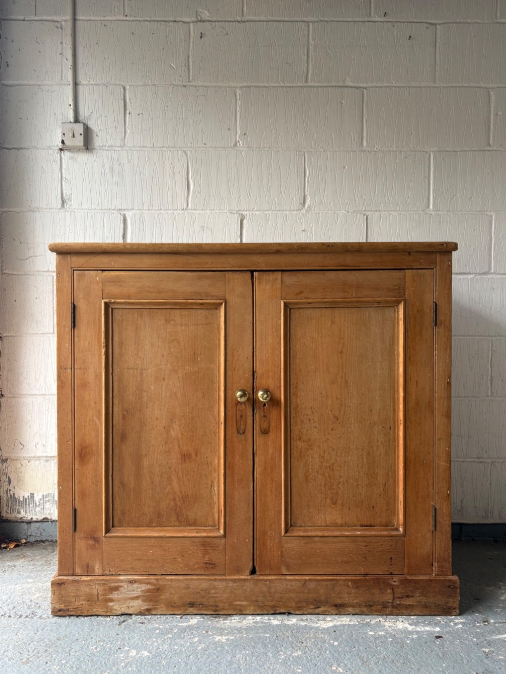 A nineteenth-century Victorian pine two-door cupboard featuring recessed panel doors, brass knobs, and a solid plinth base.