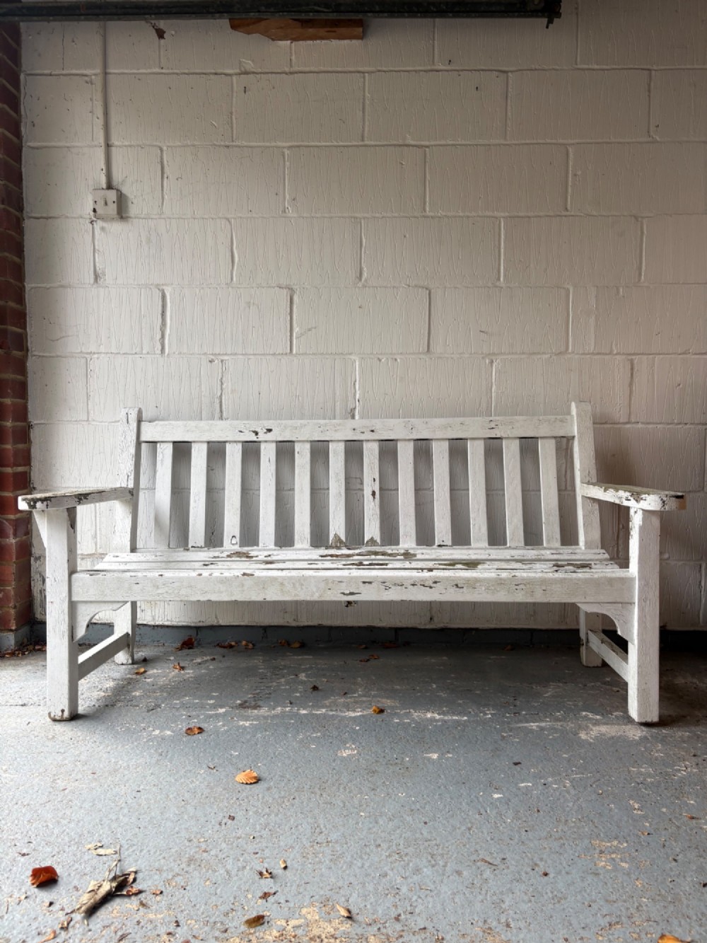 An early 20th-century teak garden bench with a vertical slatted backrest, flat armrests, and a weathered white painted finish.