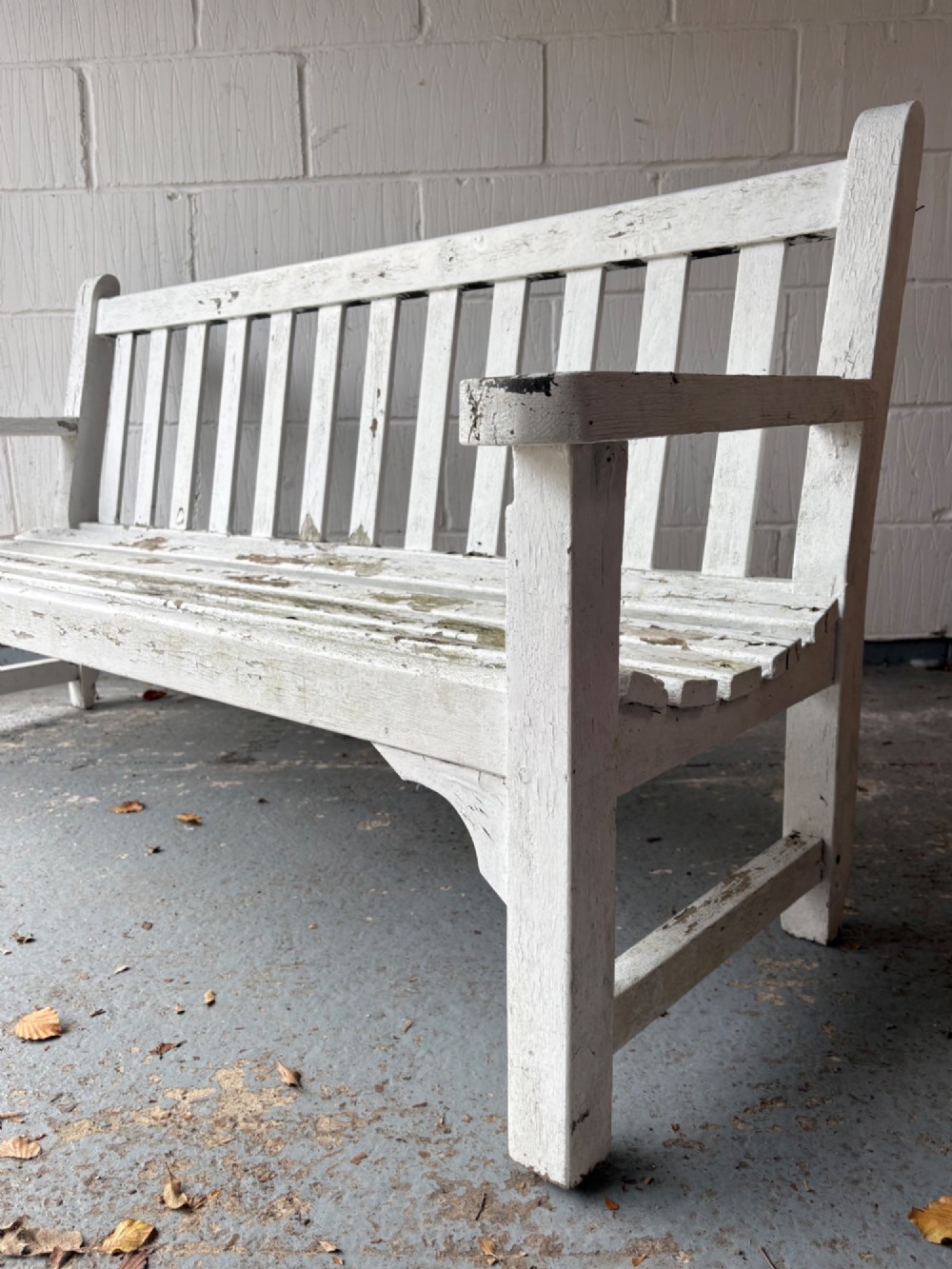 An early 20th-century teak garden bench with a vertical slatted backrest, flat armrests, and a weathered white painted finish. View II