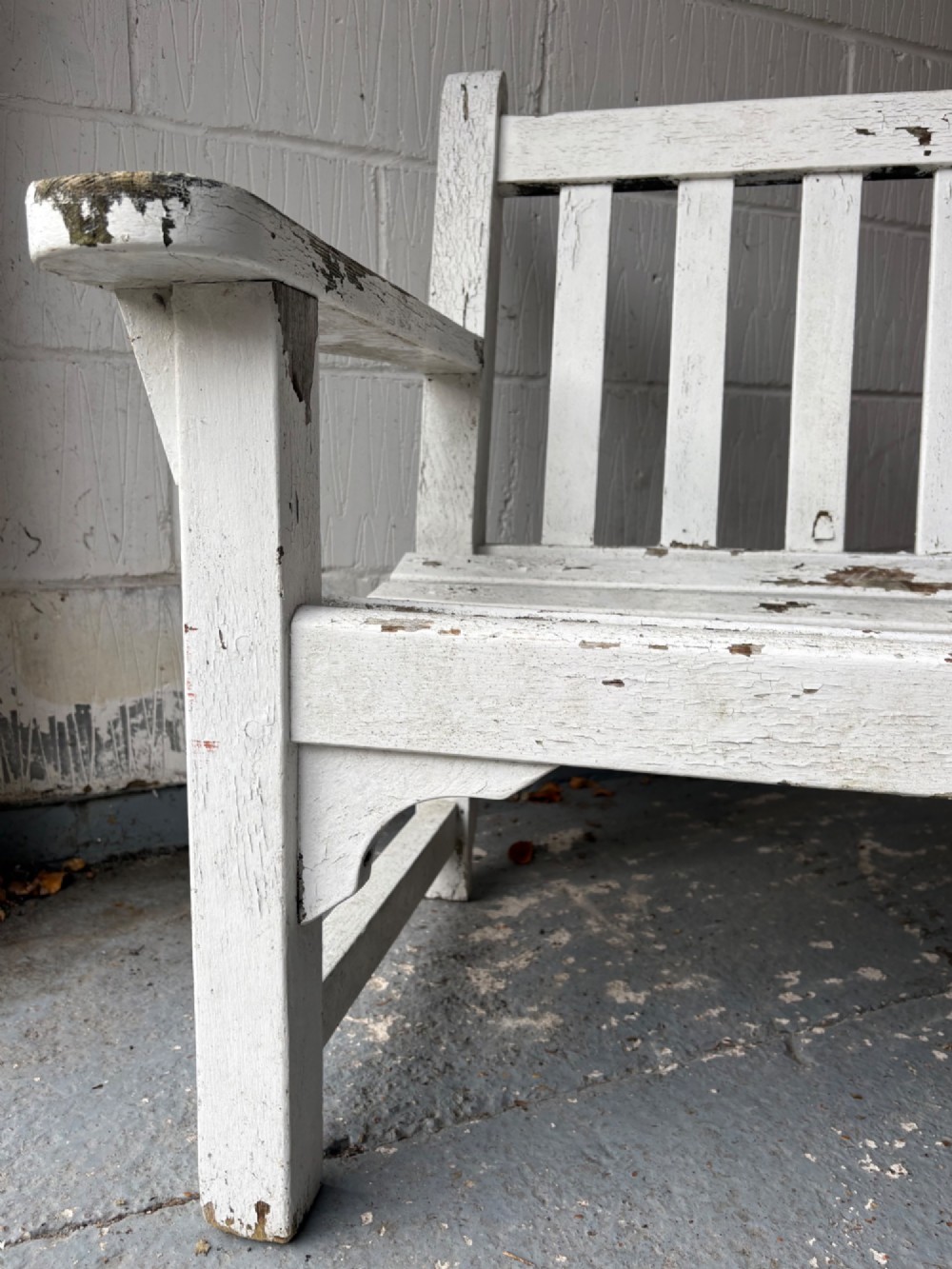 An early 20th-century teak garden bench with a vertical slatted backrest, flat armrests, and a weathered white painted finish. View III