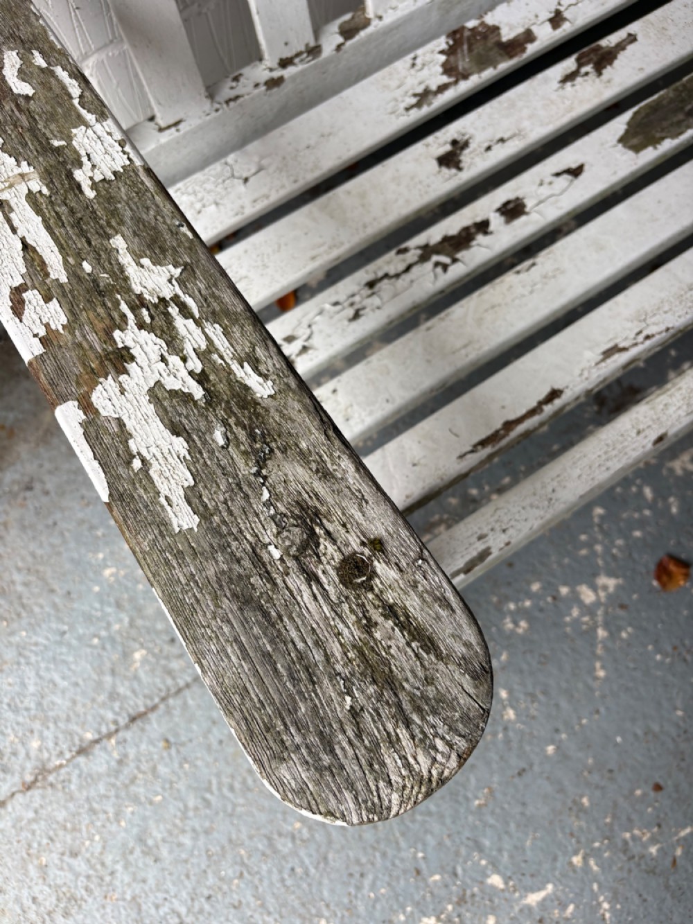 An early 20th-century teak garden bench with a vertical slatted backrest, flat armrests, and a weathered white painted finish. View V