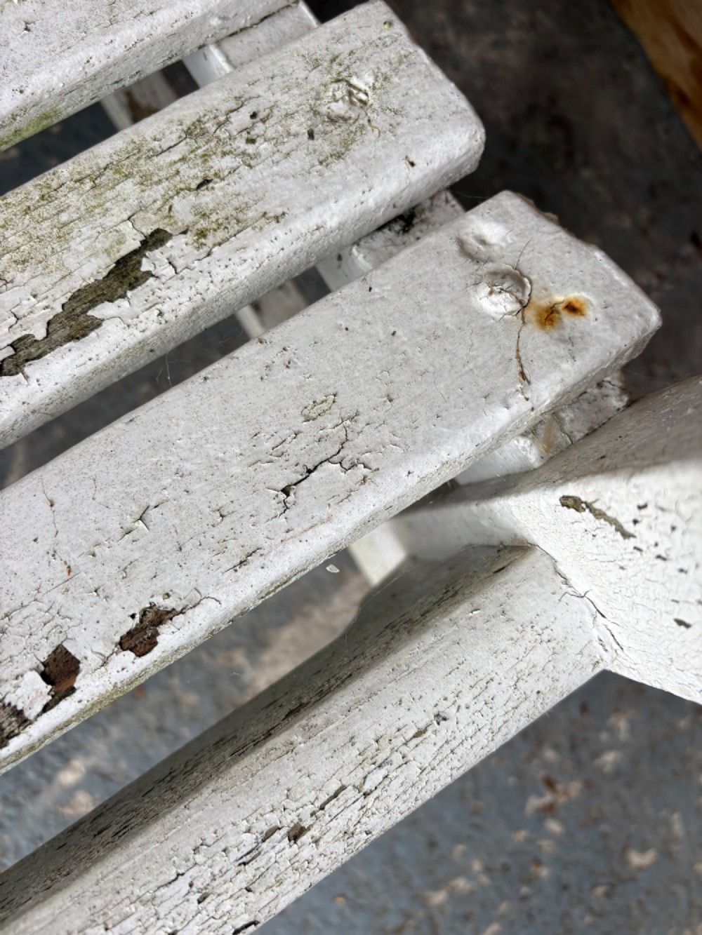 An early 20th-century teak garden bench with a vertical slatted backrest, flat armrests, and a weathered white painted finish. View VI
