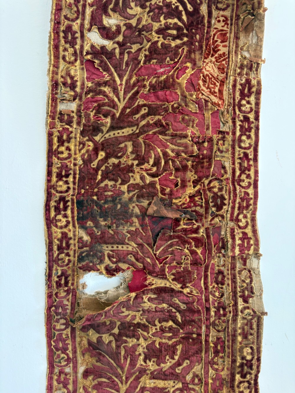 A long vertical 17th-century Italian crimson velvet textile fragment with gold silk acanthus leaf embroidery and patterned borders. View IV