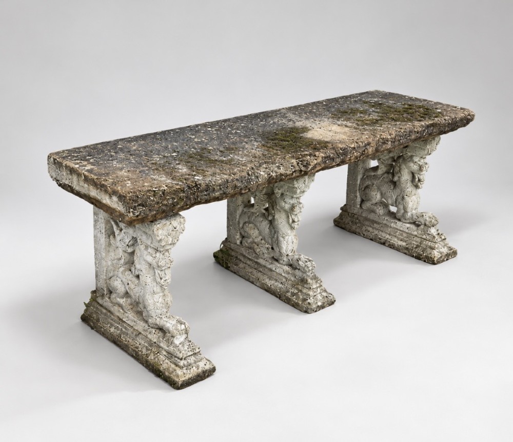 A weathered stone garden bench featuring a rectangular York stone top resting on three cast stone griffin pedestals.