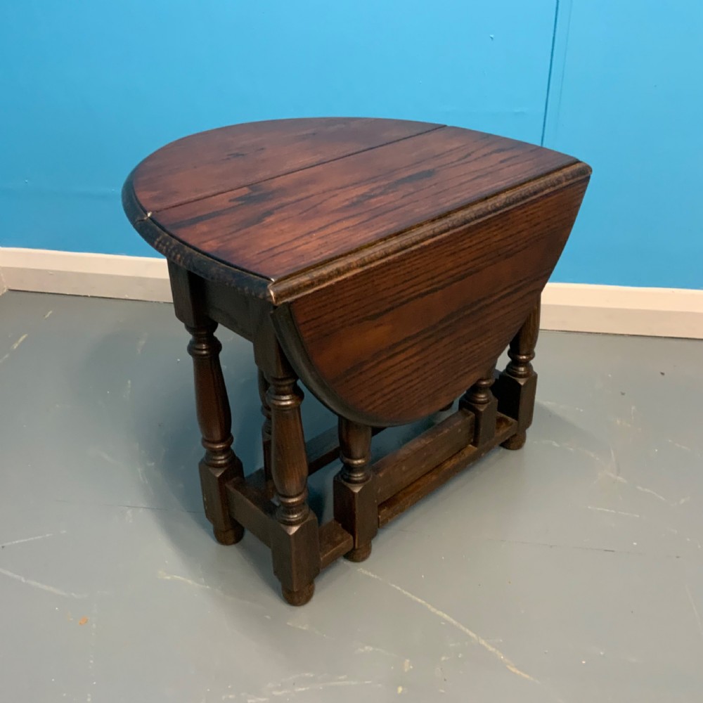 A dark oak gateleg side table featuring turned baluster legs, base stretchers, and hinged drop-leaf sides.