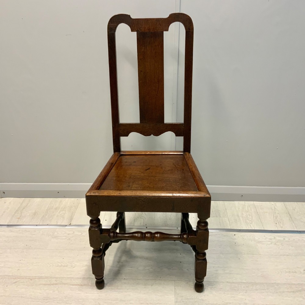 A late 17th-century dark oak back stool side chair featuring a solid wooden seat, central back splat, and turned front legs with stretchers.