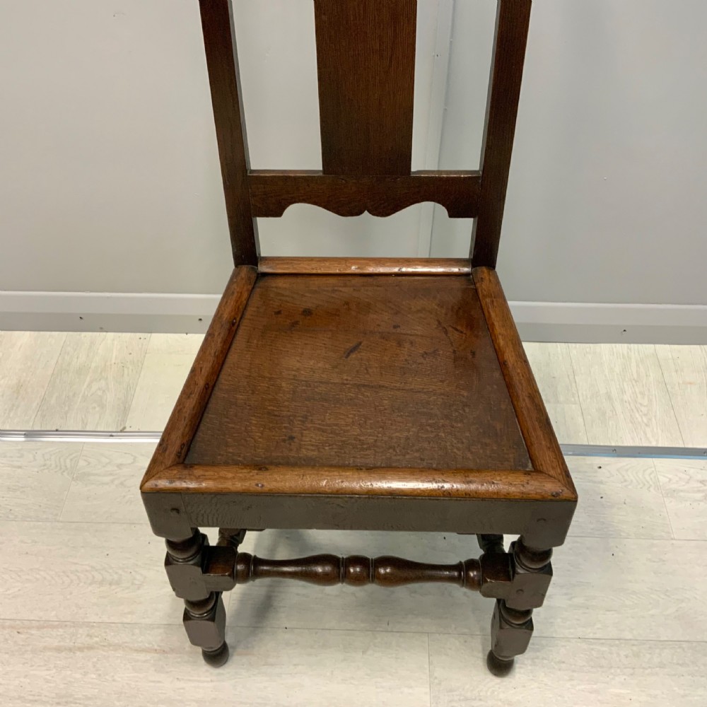A late 17th-century dark oak back stool side chair featuring a solid wooden seat, central back splat, and turned front legs with stretchers. View II