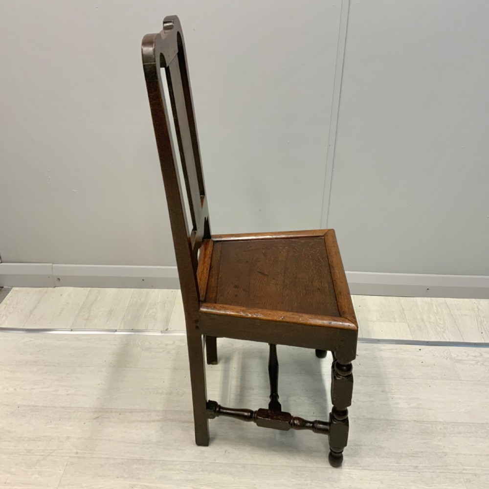 A late 17th-century dark oak back stool side chair featuring a solid wooden seat, central back splat, and turned front legs with stretchers. View V