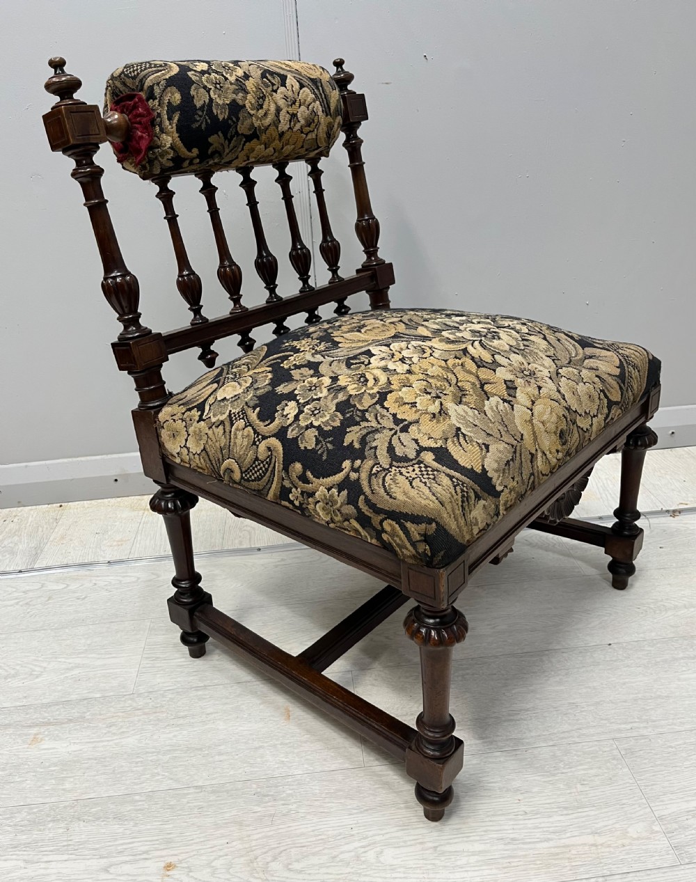A Victorian low-seated prie-dieu prayer chair featuring turned wooden legs, a spindle back gallery, and black and gold floral tapestry fabric.