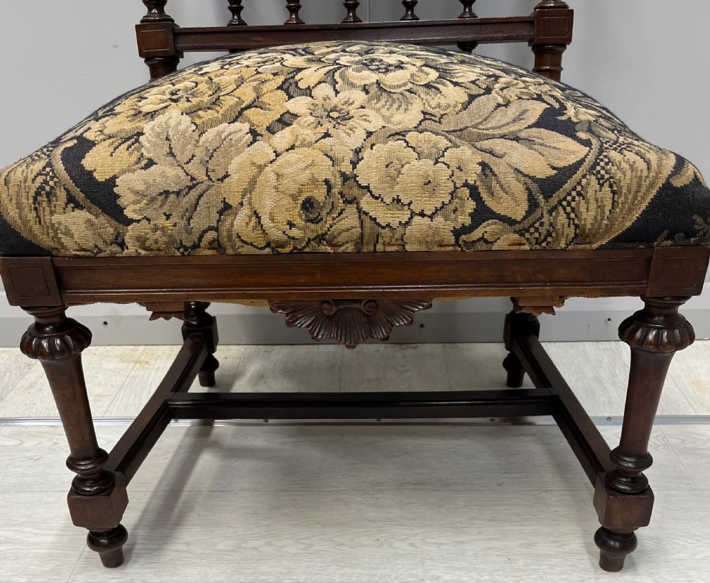 A Victorian low-seated prie-dieu prayer chair featuring turned wooden legs, a spindle back gallery, and black and gold floral tapestry fabric. View V