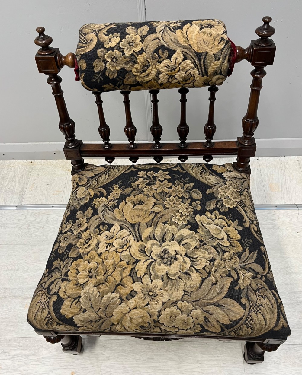 A Victorian low-seated prie-dieu prayer chair featuring turned wooden legs, a spindle back gallery, and black and gold floral tapestry fabric. View VI