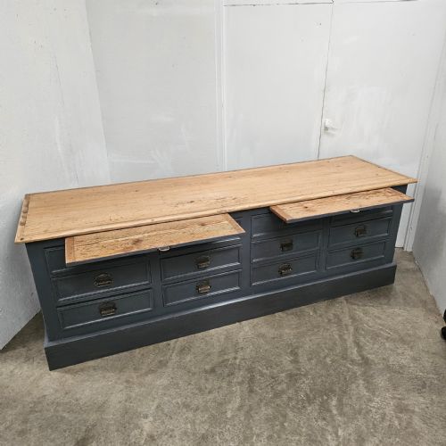 fig 2. A long French shop counter featuring twelve drawers painted in dark grey with metal cup handles and a natural scrubbed pine top surface.