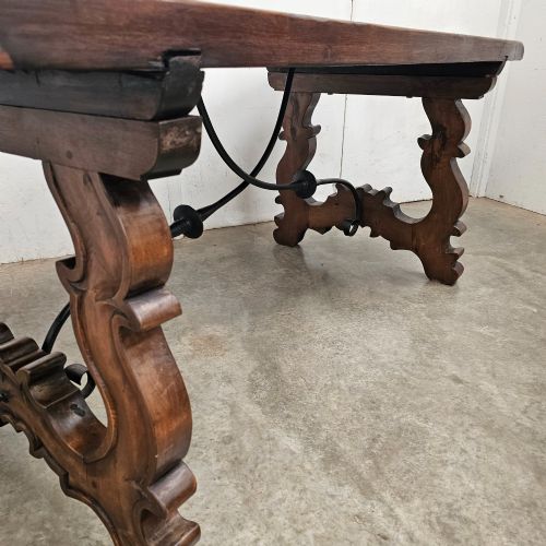 fig 1. A dark brown rectangular wooden dining table with carved trestle legs connected by curved wrought iron stretchers.