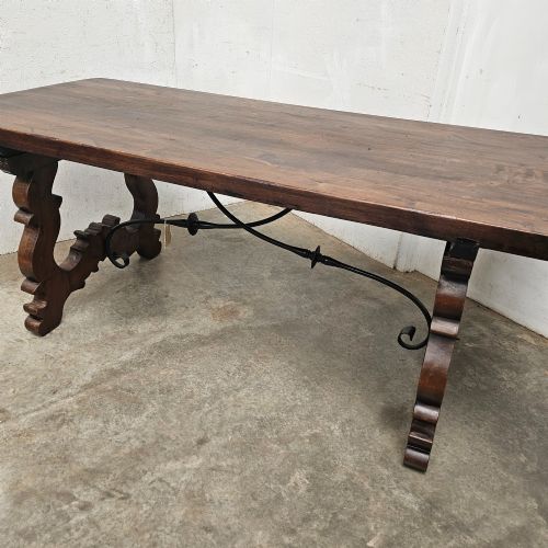 fig 2. A dark brown rectangular wooden dining table with carved trestle legs connected by curved wrought iron stretchers.