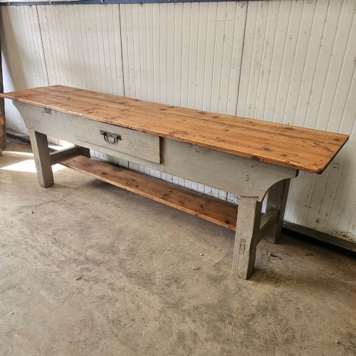 fig 1. A long rustic pine worktable featuring a natural wood top, a light grey painted frame with a single drawer, and a lower shelf.