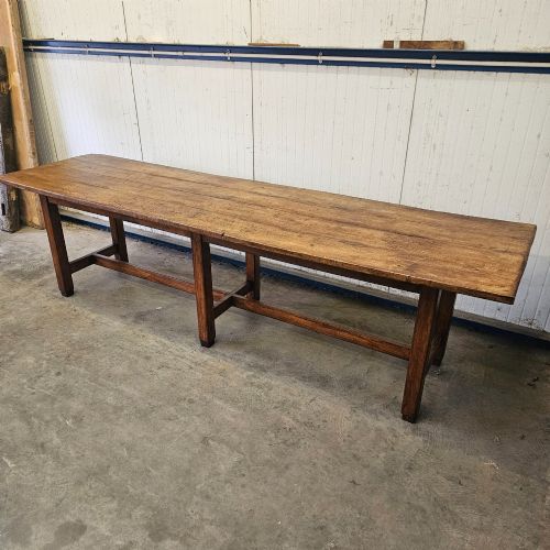 fig 1. An extra long French beechwood table featuring a plank top, six square legs, and supporting stretchers in a warm brown timber finish.
