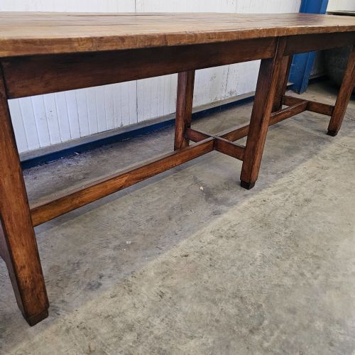 fig 2. An extra long French beechwood table featuring a plank top, six square legs, and supporting stretchers in a warm brown timber finish.
