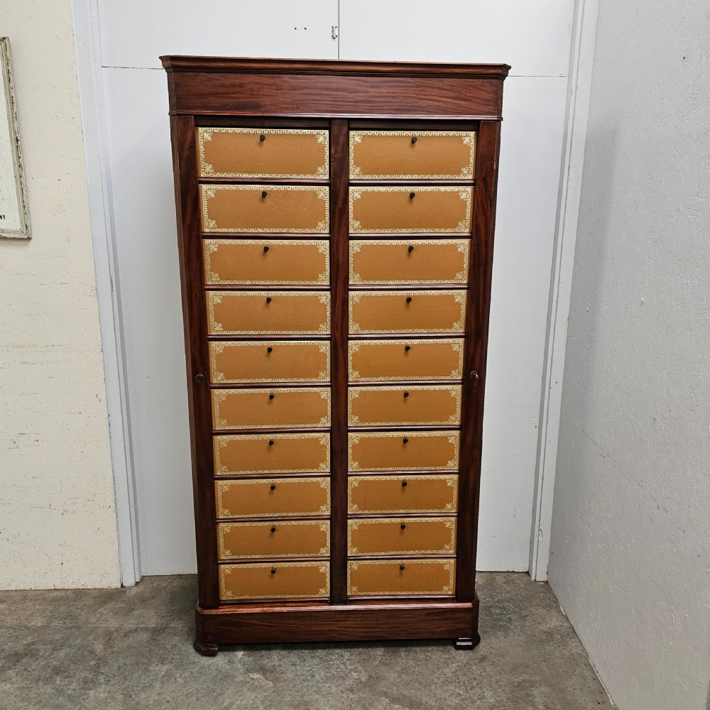 A tall French mahogany cartonnier cabinet with two vertical columns of drop-front drawers featuring gilt-tooled tan leather fronts.