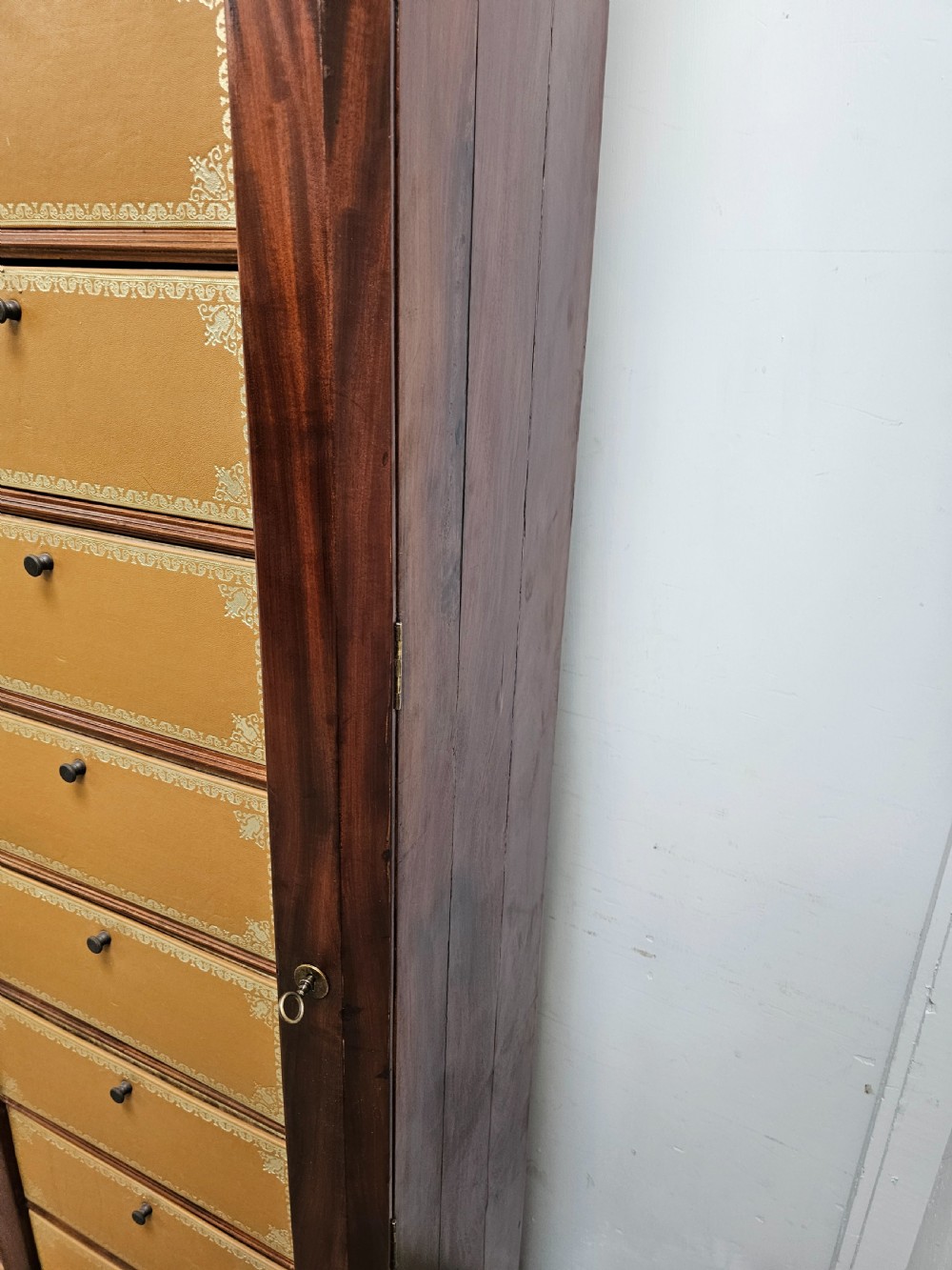A tall French mahogany cartonnier cabinet with two vertical columns of drop-front drawers featuring gilt-tooled tan leather fronts. View V