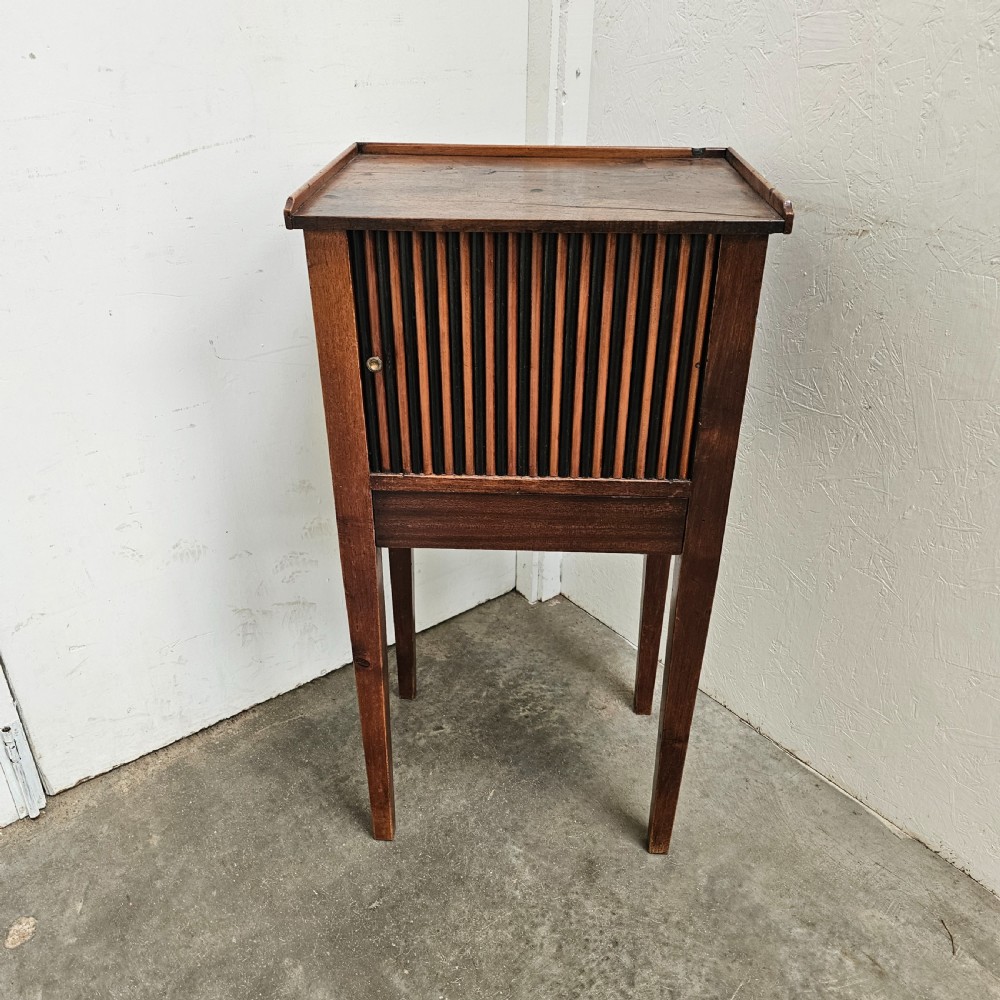 A tall walnut bedside cabinet featuring a vertical tambour slatted door, square tapered legs, and a raised gallery top.