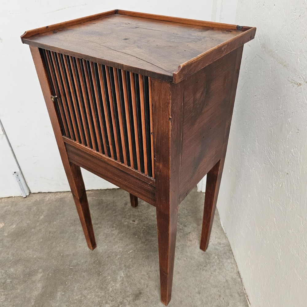 A tall walnut bedside cabinet featuring a vertical tambour slatted door, square tapered legs, and a raised gallery top. View IV
