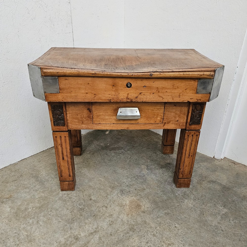 An antique French beech butchers block featuring a dished top surface, metal corner brackets, a single drawer, and carved square legs.