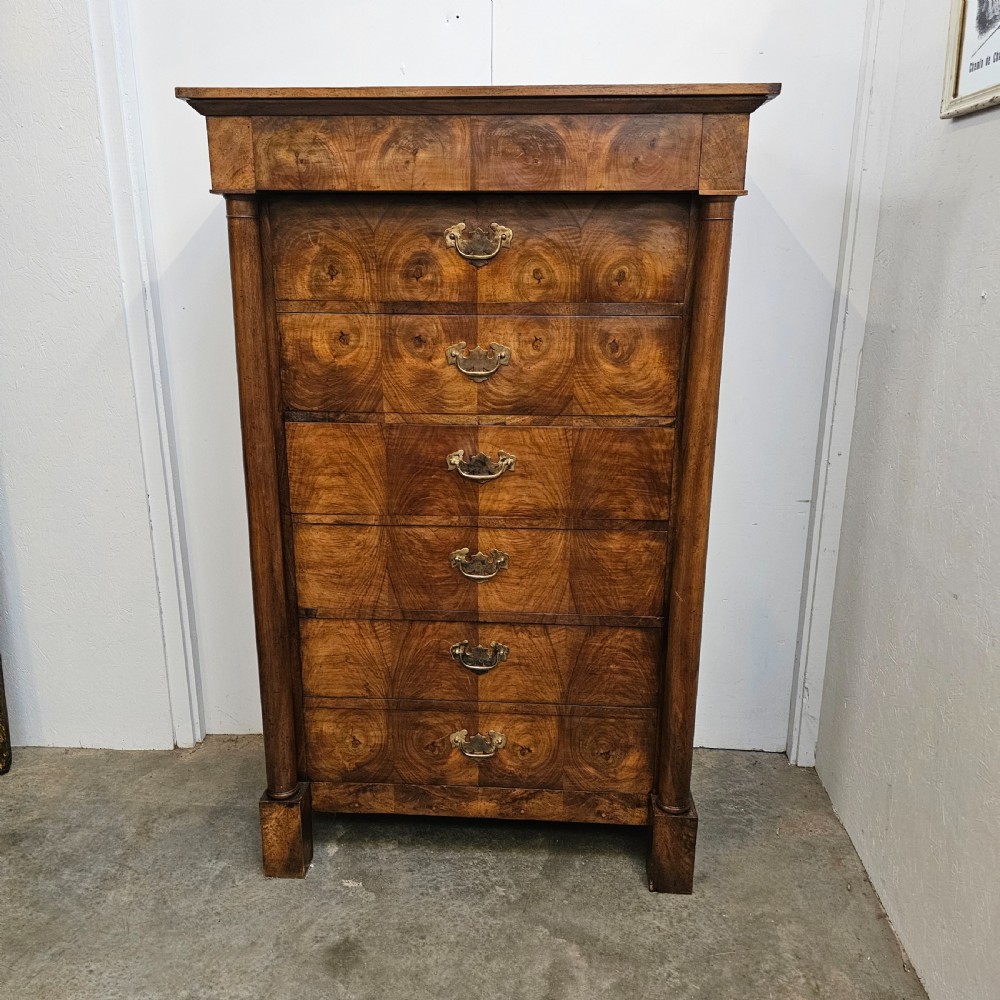 A tall 19th-century French Empire chest of drawers featuring bookmatched walnut grain veneer, flank column pilasters, and six stacked drawers with brass bail handles.