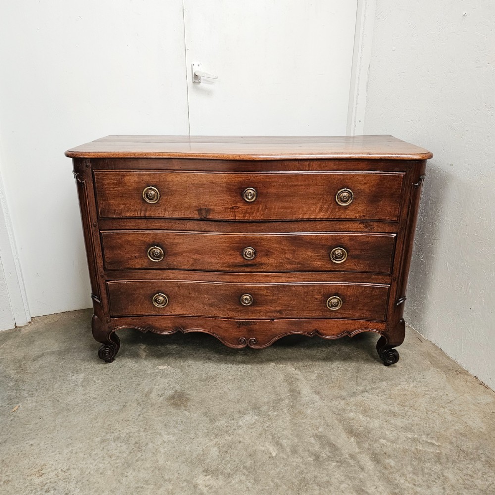 A nineteenth-century French serpentine wood commode featuring three drawers with brass ring handles and carved cabriole legs.