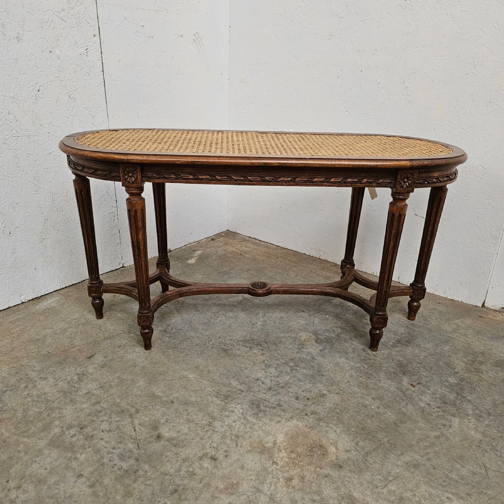 An oval French carved beech banquette with a hand-woven cane seat, fluted legs, carved rosettes, and an X-form stretcher.