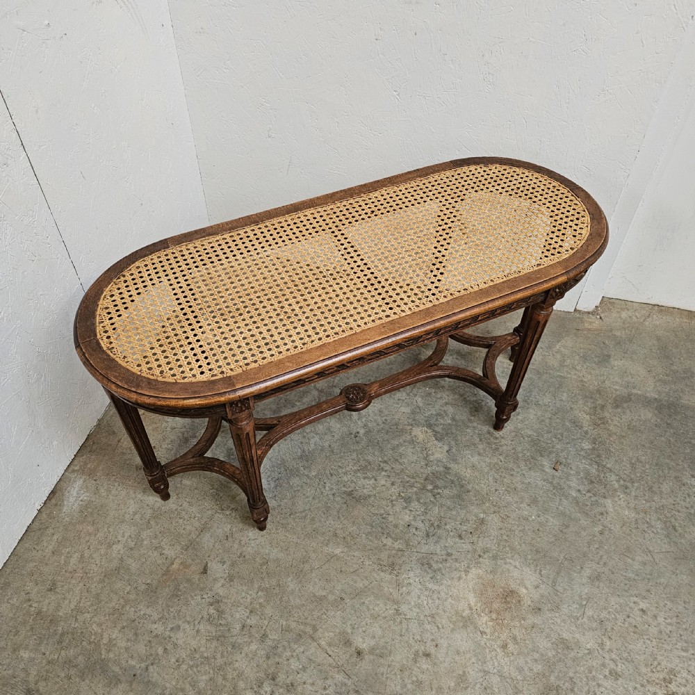 An oval French carved beech banquette with a hand-woven cane seat, fluted legs, carved rosettes, and an X-form stretcher. View II
