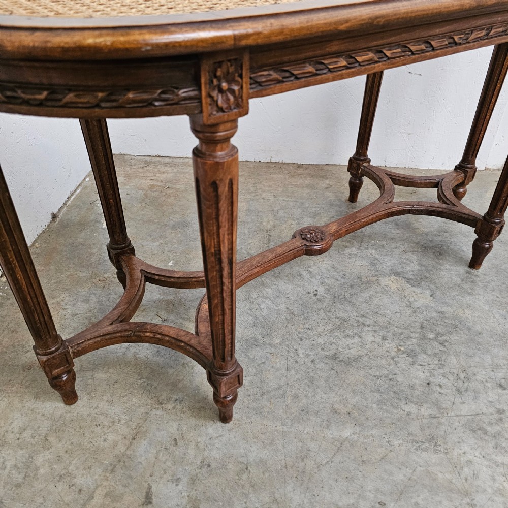 An oval French carved beech banquette with a hand-woven cane seat, fluted legs, carved rosettes, and an X-form stretcher. View III