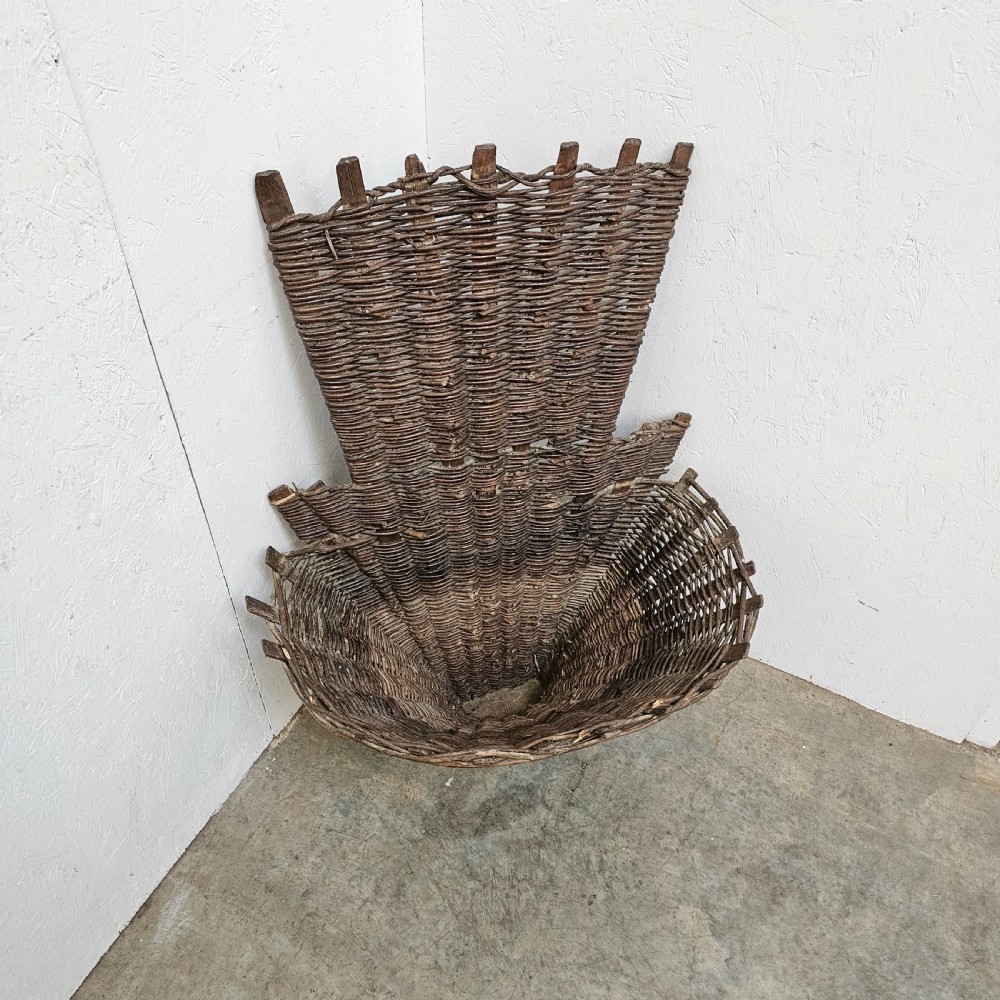 An antique French wicker grape harvester basket featuring a flared woven willow container resting on a wooden base with an extended vertical backrest. View III