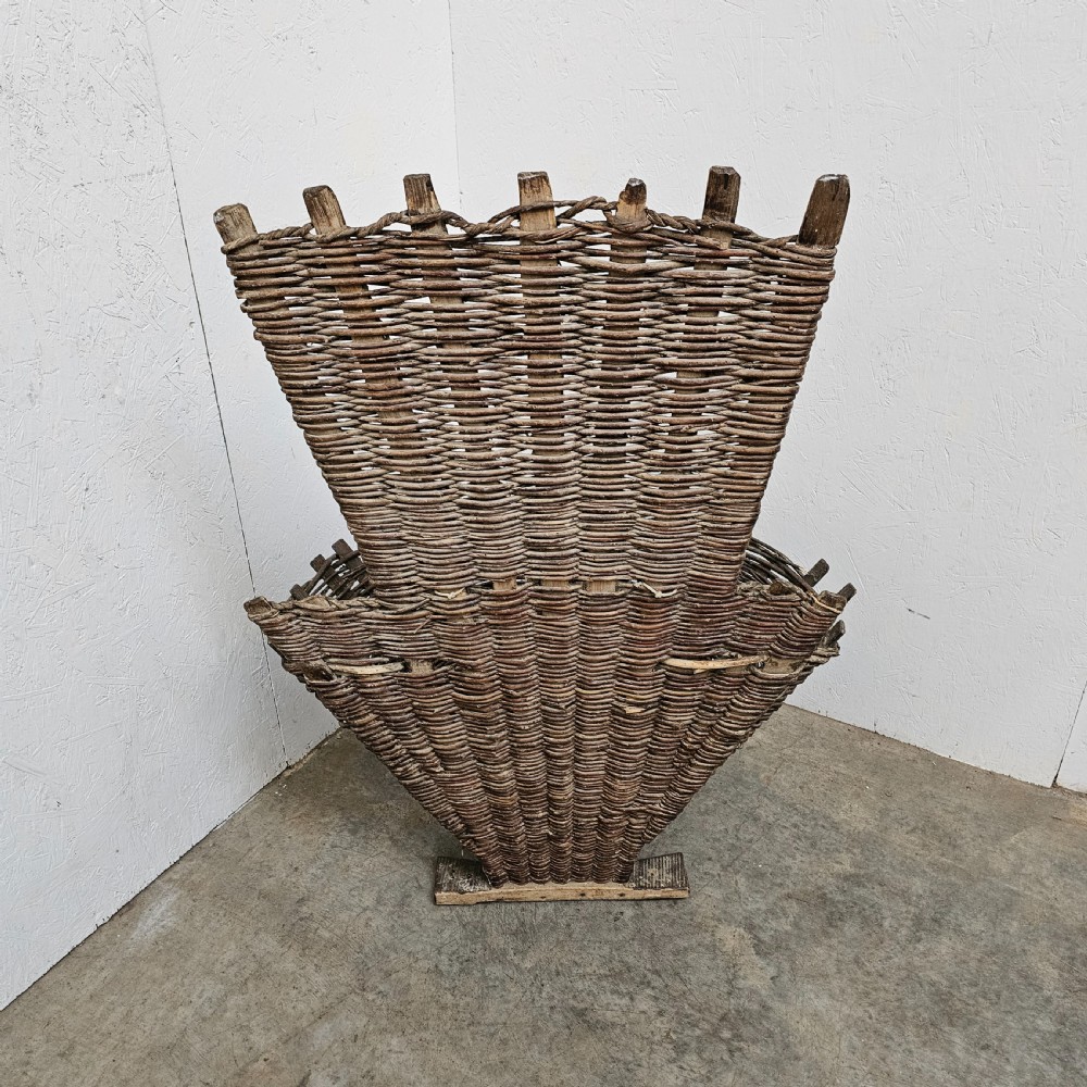 An antique French wicker grape harvester basket featuring a flared woven willow container resting on a wooden base with an extended vertical backrest. View IV