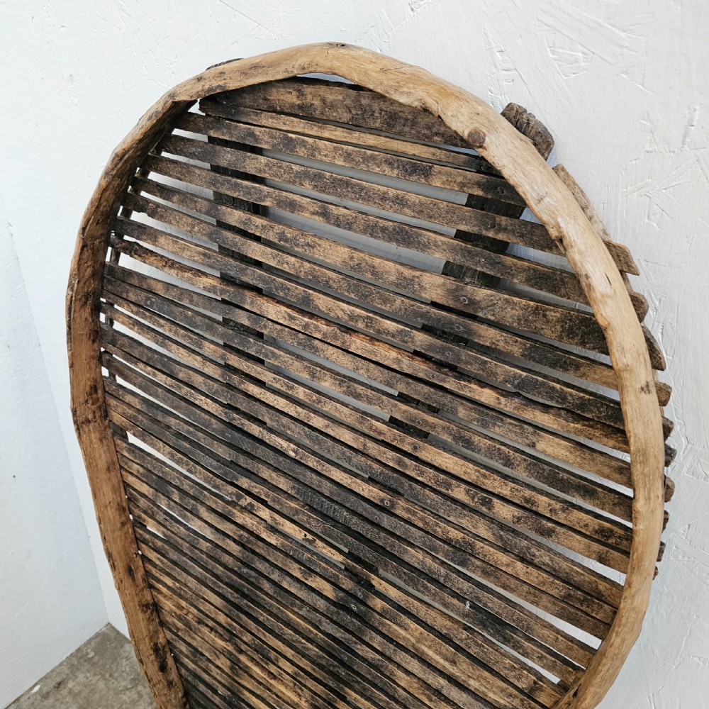 A teardrop-shaped French cleft hazel prune drying rack with horizontal wooden slats within a curved timber frame. View III