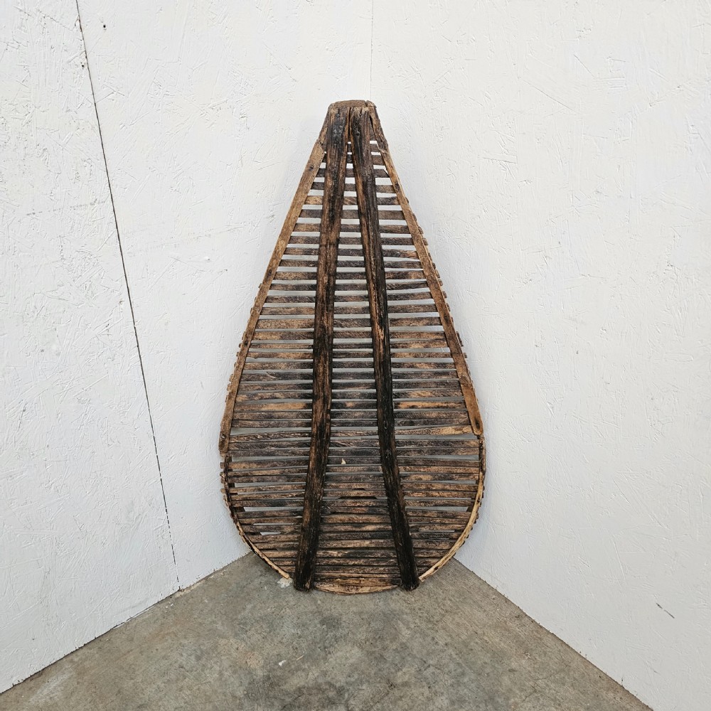 A teardrop-shaped French cleft hazel prune drying rack with horizontal wooden slats within a curved timber frame. View VI